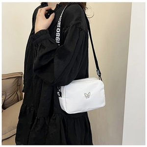 Detailed view of white nylon crossbody bag featuring silver butterfly and 1980 strap