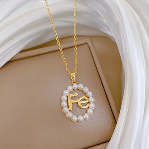 Macro detail of gold pearl pendant with FE letter emblem on delicate link chain necklace