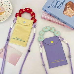Flat lay of small embroidered canvas phone bags in yellow and purple with wavy handles