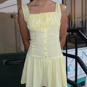 Detailed view of pale yellow sleeveless dress with button front and pleated tie-up chest