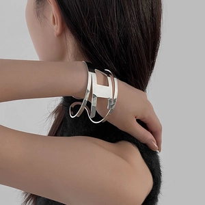 Minimalist silver metal hollow geometric cuff bracelet worn by a model on a grey background