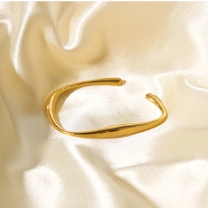 Close-up of golden irregular wave open bangle on elegant champagne silk fabric background