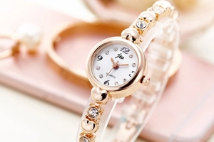 Macro detail of gold watch with white dial, crystal markers, and heart chain links