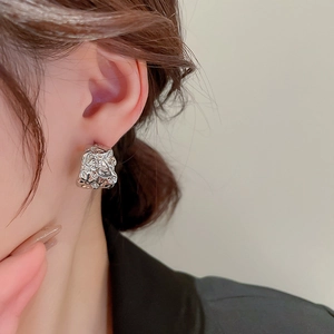 Close-up of irregular textured silver earrings with a crinkled metal lava finish