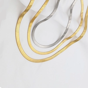 Detailed flat lay of gold and silver herringbone chains on white wrinkled fabric