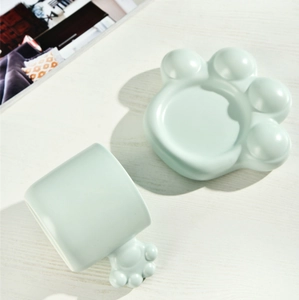 Detail of light green ceramic cat paw shaped cup and saucer set on white wooden table