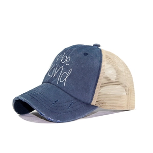 Detail of 'be kind' embroidery and heart on a distressed navy and beige mesh baseball cap