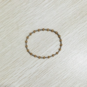 Detailed top view of 18K gold and silver elastic beaded bracelet on a wood background