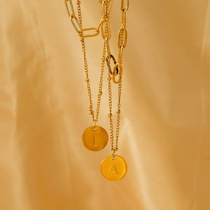 Gold double-layer paperclip necklace with initial pendants on soft fabric backdrop