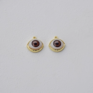 Macro detail of two gold-plated eye charms with brown pupils and white iris details