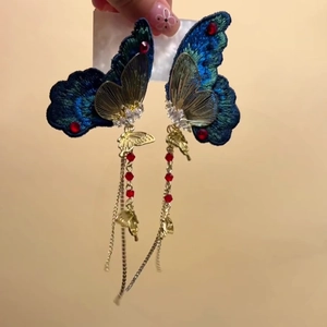 Detail of embroidered butterfly tassel earrings with blue gradient wings and red beads