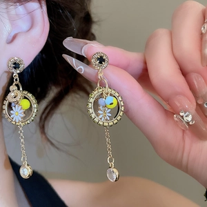 Close-up of golden tassel earrings with daisy motif, colored beads and zircon detail