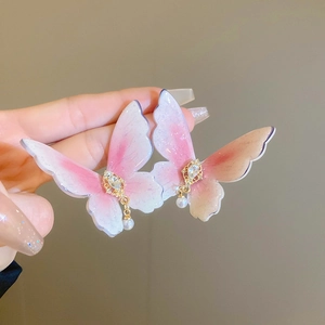 Close-up of butterfly stud earrings with pink glitter wings and pearl drops