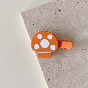 Close-up of cute orange mushroom hair clip with white dots on a natural stone background