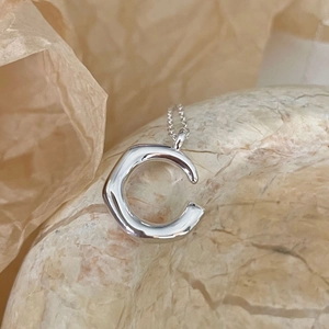 Polished silver 925 irregular C-shaped pendant necklace on a textured stone base