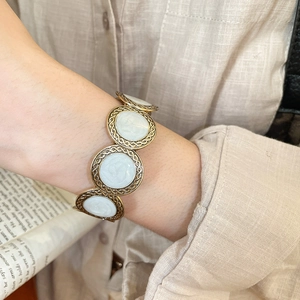 Close-up of retro gold-tone round charm bracelet with white inlay and rope texture details