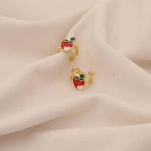 Detail of red strawberry ear cuffs with gold finish on soft beige fabric background