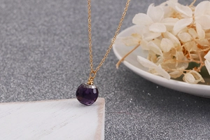 Macro detail of purple faceted crystal pendant on a gold titanium steel necklace
