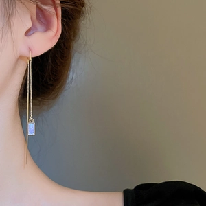 Elegant gold drop chain earrings with rectangular purple opal stones on a model