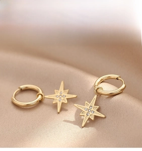 Close-up of golden eight-pointed star earrings with crystals on champagne silk background