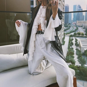 Close-up of white ruffled chiffon blouse with black leather blazer and city skyline backdrop