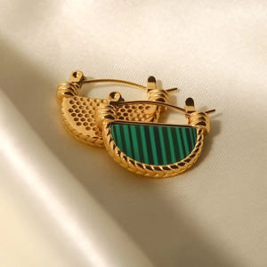 Macro-opname van gouden vintage oorbellen met groen malachietpatroon op zijde