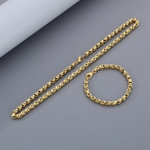 Détail d'un ensemble collier et bracelet chaîne byzantine dorée sur fond gris mat