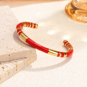 Luxe red enamel and gold stainless steel cuff bracelet on textured stone background