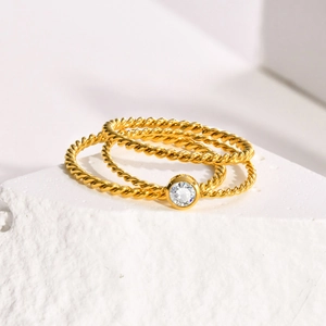 Close-up of three twisted gold rings with a round bezel-set zircon on stone