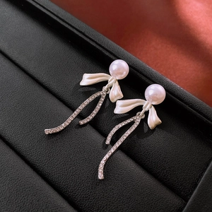 Detail of bow-shaped earrings with faux pearl and curved rhinestone tassel on black leather