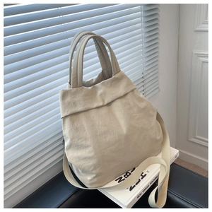 Detail of beige nylon tote bag with wide handles and adjustable strap on lifestyle backdrop