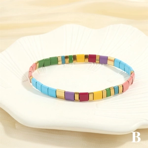 Detail of colorful enamel Tila bead elastic bracelet in a white ceramic petal tray