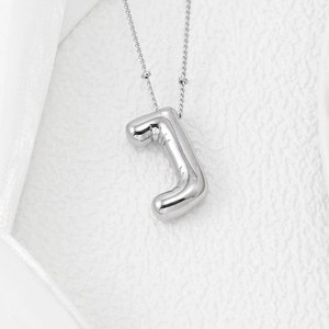 Macro shot of silver balloon letter J pendant with beaded chain on white velvet