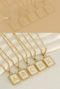 Close-up of golden rectangular letter pendant with white shell and inlaid diamonds