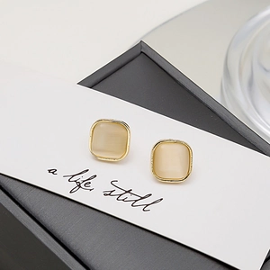 Detail of square cat-eye stone earrings with gold metal frame on a white card