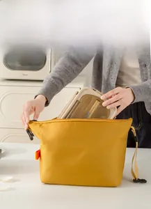 Detail of placing a lunch box into the insulated yellow canvas bento bag with foil lining
