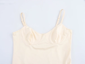 Detail of elegant beige camisole dress showing thin straps and structured cups on white background