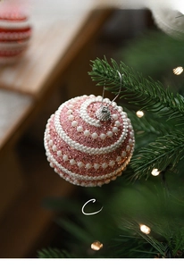 Pink glitter Christmas ball with white pearl swirls hanging on a festive tree branch