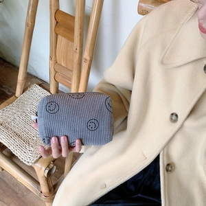 Macro shot of grey corduroy makeup bag with smiley face print held by hand
