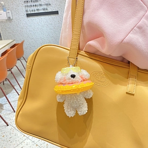Dettaglio di un simpatico ciondolo a forma di cane bianco con occhiali su borsa gialla