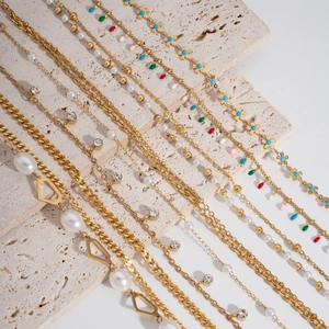 Detailed close-up of double-layer gold pearl anklets on a textured beige stone surface