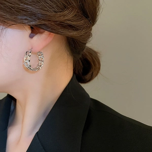 Close-up of interlocking silver chain earrings with pavé zircons worn on a model
