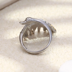 Close-up of a silver swan ring with small white diamonds on a beige stone texture