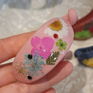 Pink resin hair clip with dried flowers and rhinestones, shown in a hand-held close-up shot