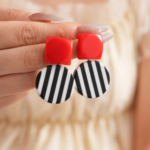 Detail of geometric earrings with red square studs and black and white striped resin pendants