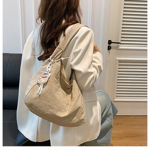 Beige pleated nylon hobo shoulder bag shown on model in a cozy minimalist interior