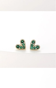 Close-up of golden heart earrings with emerald green crystals on white pedestal