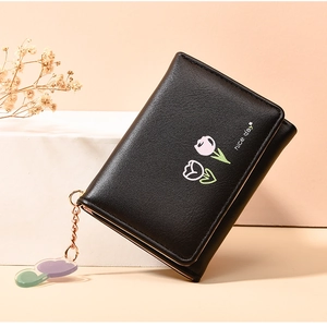 Detail of black faux leather wallet with tulip embroidery and a gold floral pendant charm