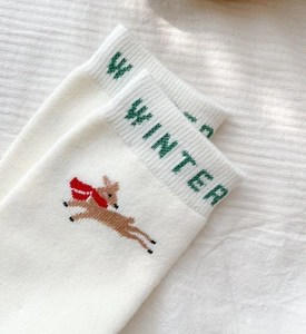 Close-up of white winter sock featuring a brown reindeer embroidery and green text detail