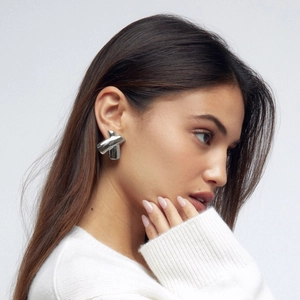 Polished silver stainless steel chubby X-shaped earrings worn by a model on a grey background